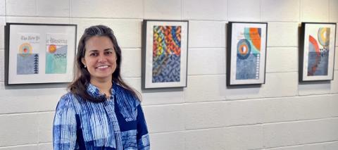 Photograph of the artist, Anjelika Deogirikar Grossman, with her artwork on display in the Gelardin Center Exhibit Area on the first floor of Lauinger Library 