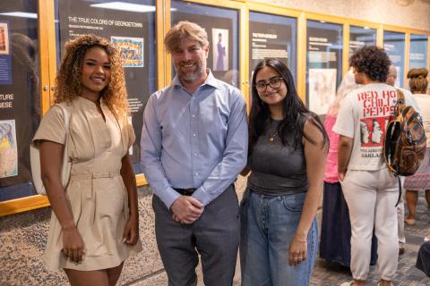A white professor poses next to two female student artists in front of their artwork.