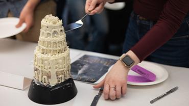 A hand cuts through a cake modeled after the titular tower from RF Kuang's Babel.