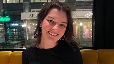 A white female student smiles in a booth at a restaurant.