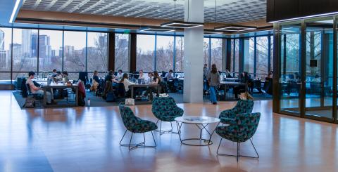 Wide view of the renovated Pierce Reading Room, featuring long, polished wooden study tables lined with classic reading lamps, high ceilings, large windows, and students studying, reading, and talking..