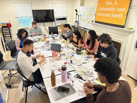 Group of participants around a big table filled with magazines, scissors, glue sticks and art supplies creating zines filled with collages.