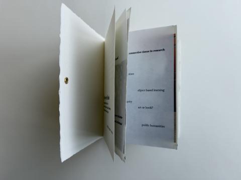 An artists’ book that’s opening so that you can see some of the pages insides that are filled with text and photos.