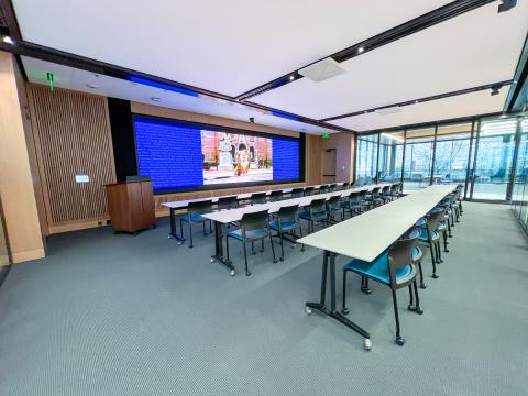 Wide view of the renovated Duran Visualization and Learning Lab, featuring long white study tables lined with blue roller chairs, high ceilings, and large glass windows.