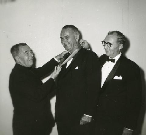 Black and white photograph showing GU President Edward B. Bunn, S.J., placing the John Carroll Medal on a ribbon around the neck of Lyndon Johnson
