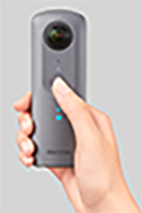 The Ricoh Theta V camera being held by a hand.