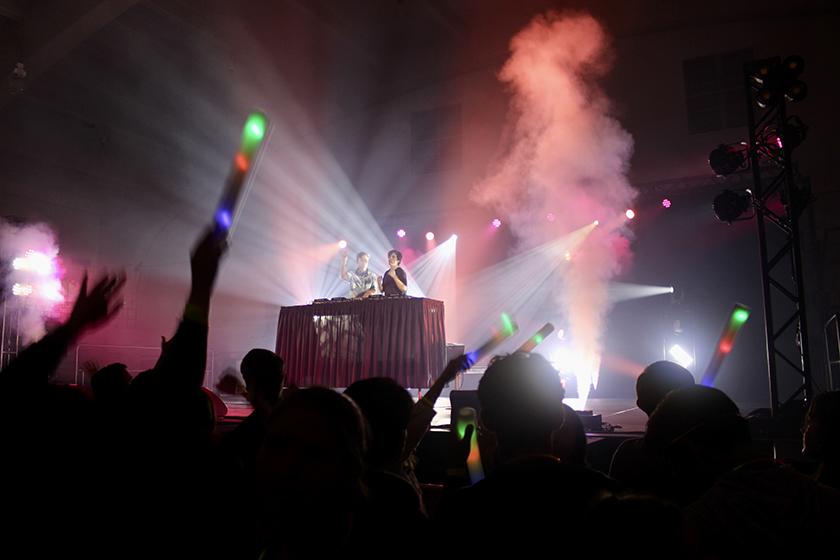 Two DJs with their hands up towards the crowd. 