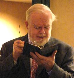 Dr. Betz holds his glasses in one hand while reading from a book at a Library Board Meeting