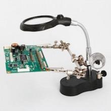 A circuit board is clipped to a stand below a magnifying glass