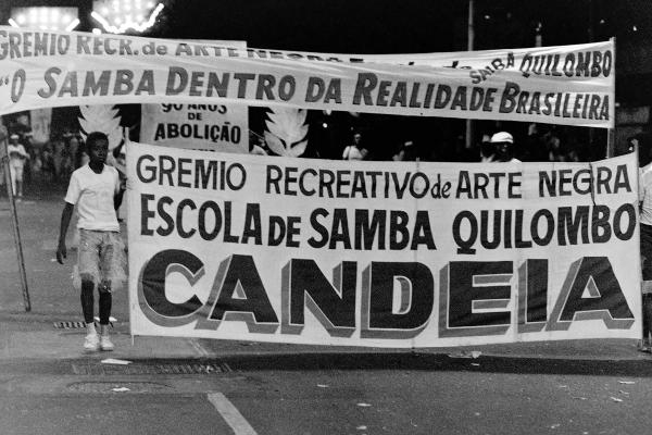Black and white photo of a kid holding one side of a big banner in a street parade.