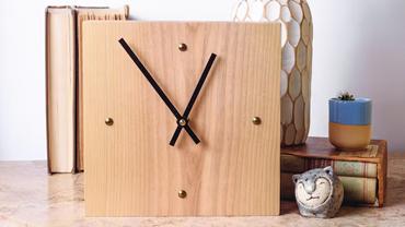 a square, simple wooden clock sitting on a shelf