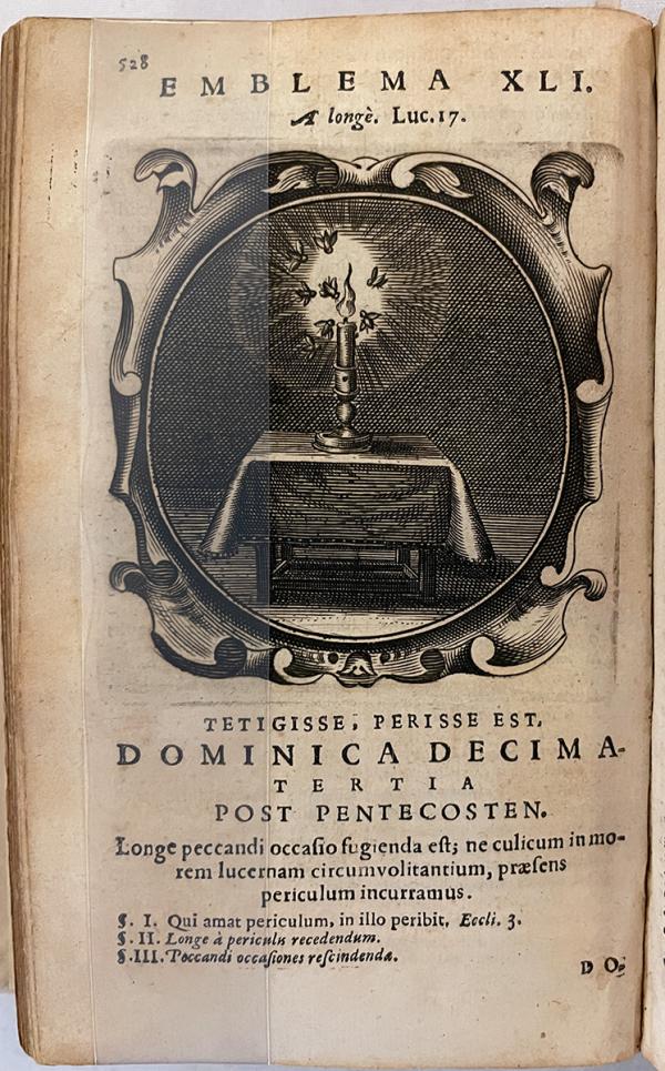 A lone candle sits on a table while small insects surround the flame.