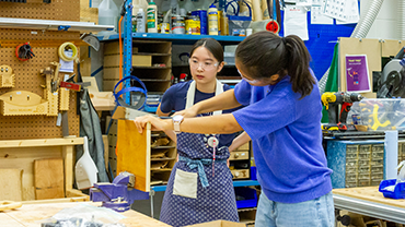 two students cutting a piece of wood with a hand saw