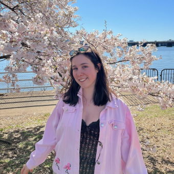 woman in pink shirt stands under a flowering cherry tree