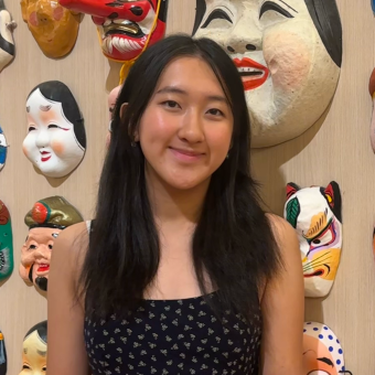 woman standing and smiling in front of a wall of masks