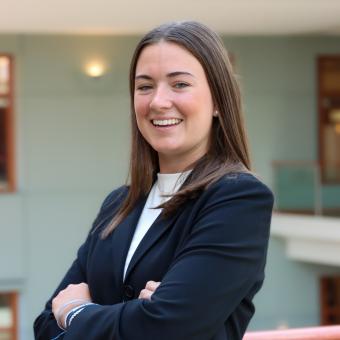 Smiling young woman with brown shoulder-length hair with her arms crossed wearing a navy suit and white shirt in Georgetown University’s McDonough School of Business.