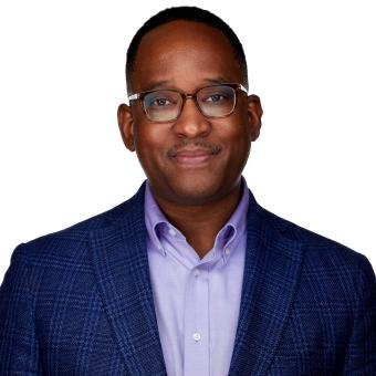 A male graduate student with black glasses wearing a navy suit and purple shirt in front of a white background.