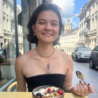 Smiling young woman with short black hair wearing a black tube top, necklace, and earrings and holding a spoon.