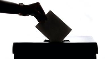 A hand putting a piece of paper into a ballot box
