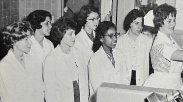 A black and white photograph from the 1960's showing 7 women in white coats