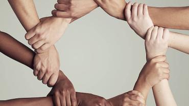 Hands and the lower arms of people with a range of skin colors adjoined in a circle.