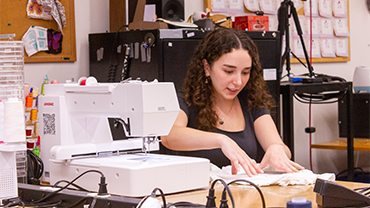 woman with brown curly hair demonstrating how to use an embroidery machine