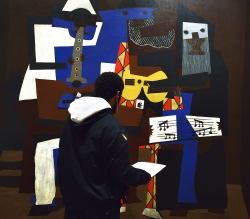 A male standing in front of Picasso's painting, Three Musicians (MOMA 1921). Due to the viewer's hooded jacket he appears to blend in with the painting. Digital photograph by Dario Zucchi.