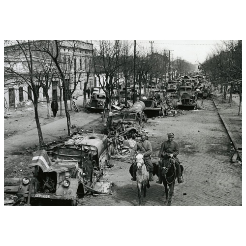 Two soldiers on horses passing a line of wrecked cars