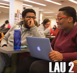 A screenshot from the Floors of Lau video, showing two students laughing, sitting at a table outside the Midnight Mug, with the text Lau 2