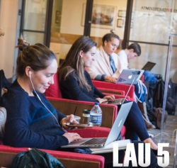 A screenshot from the Floors of Lau video, showing four students sitting in a row of chairs outside the Library's Administration offices, working on their laptops and checking their phones, with the text Lau 5