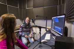 Two students in a Gelardin New Media Center editing room, each with a microphone in front of them, recording a podcast