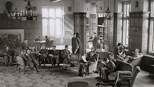 Detail from a black and white photograph of Copley Formal Lounge, in 1944. About twenty members of the Allied Services Training Program, in military uniform stand or sit in upholstered chairs and converse with each other while sunlight streams in from a south-facing window.